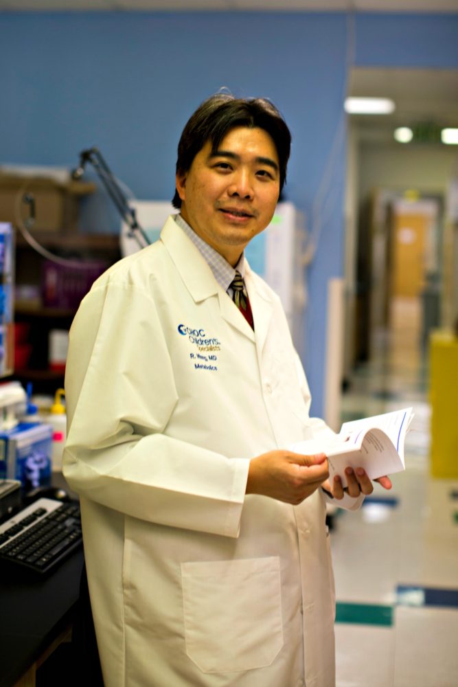 Dr. Raymond Wang, who treats patients with Batten disease, stands in lab looking over papers