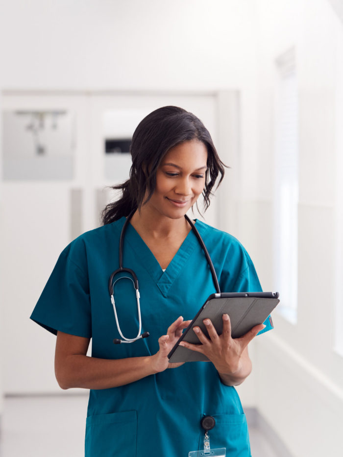 nurse Wearing Scrubs In Hospital Corridor Using Digital Tablet