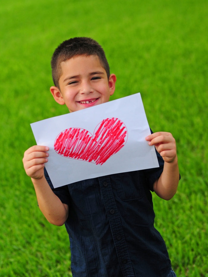 Young boy holding up a gift of a red heart drawing