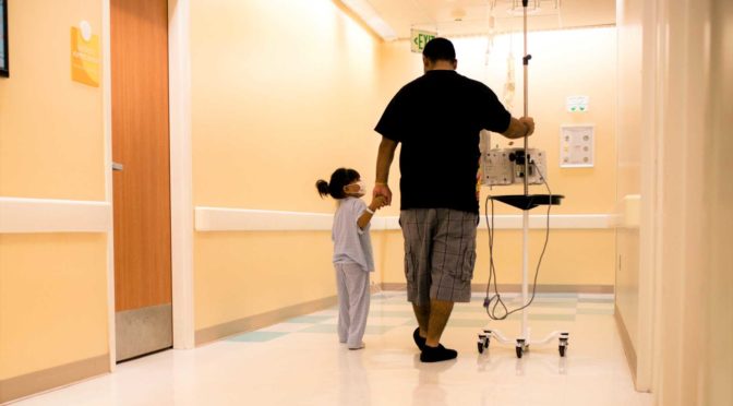 Child cancer patient and father walk through hospital