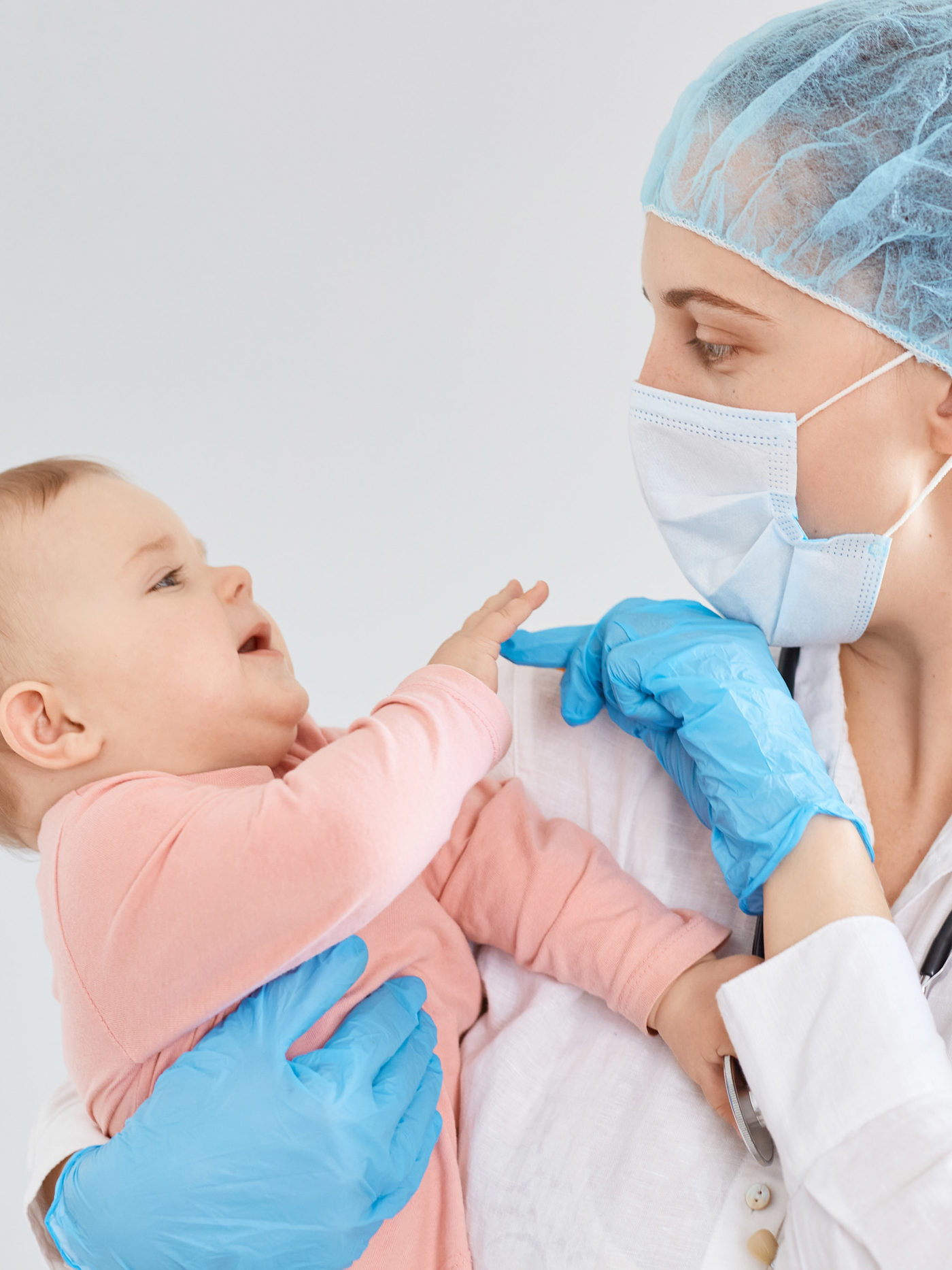 pediatrician wearing medical cap, gloves and protective mask, standing with toddler baby girl
