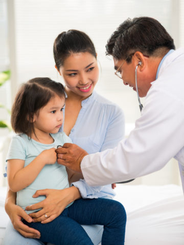 child on mom's lap gets checked out by doctor