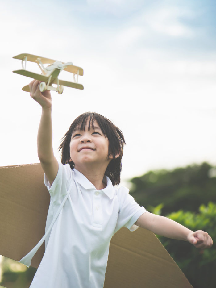 Boy with cardboard wings looks at toy airplane