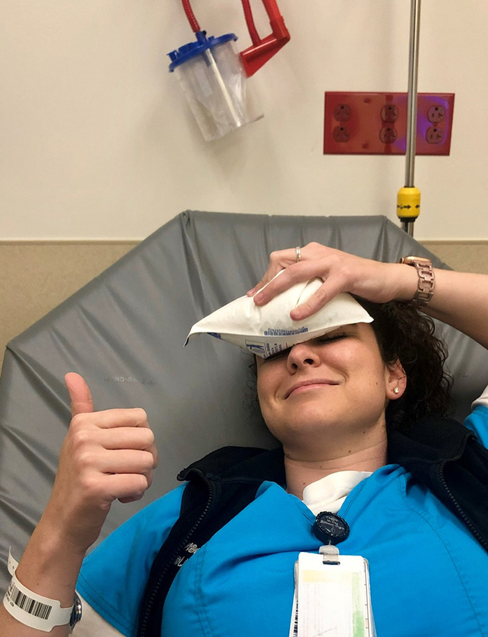 Nurse holds a thumbs up as she holds an ice pack to her head. 