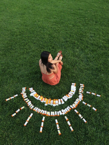 Liliana sitting in the grass with prescription medications arranged in a sun around her