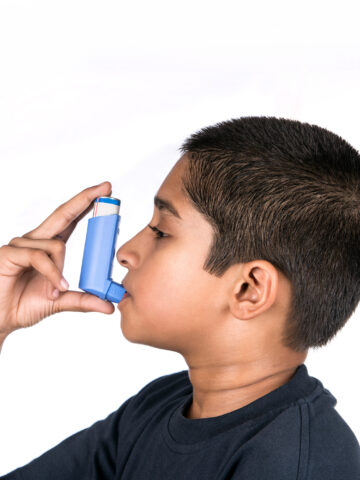 child holds inhaler to his mouth