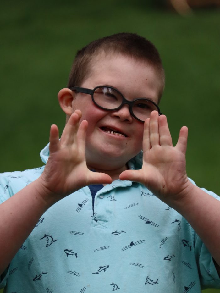 child with down syndrome holding his hands up